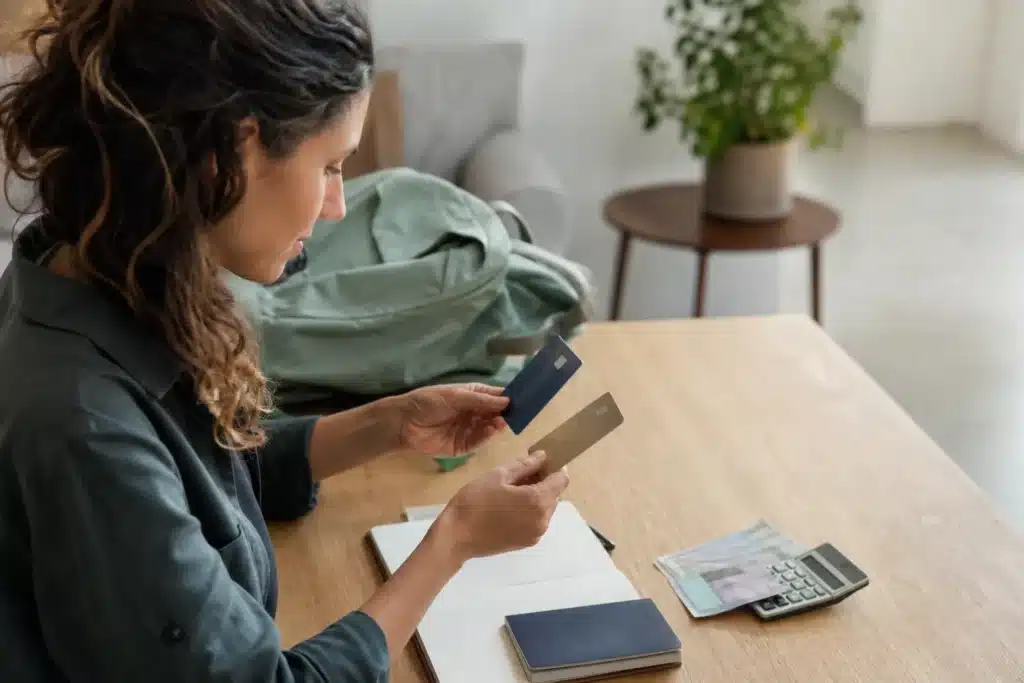 Voyageuse comparant une carte bancaire sans frais à l'étranger et une seconde carte près d’un carnet, d’un passeport fermé et de devises